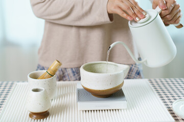 Asian woman preparing traditional Japanese matcha tea at home using bamboo tools, sifting matcha powder with care and precision.
