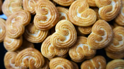Close-up view of golden brown palmier cookies arranged in a pile, featuring heart shapes and a crispy, flaky texture.
