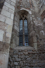 Fototapeta premium Gothic window of Corvin Castle, Romania. Tall pointed arch with stained glass framed by ancient stone walls shows medieval craftsmanship and mysterious atmosphere.