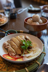Plate of poached chicken with soy and garlic dressing, garnished with cilantro and served alongside a bowl of rice balls in a traditional Asian meal