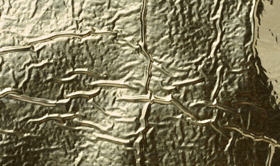 Texture of shiny gold foil with numerous wrinkles and folds.