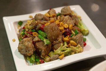 Deep-fried pork belly cubes stir-fried with peanuts, chili peppers, and green vegetables, served in a square ceramic plate