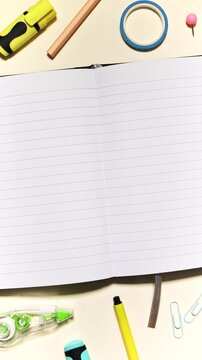 Portrait stop motion of stationery moving around an open lined notebook, leaving clear center copy space