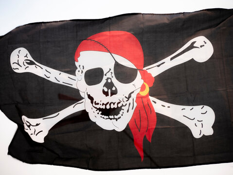 Black cloth pirate flag (Jolly Roger) featuring two tibias behind a skull with an eye patch, a golden earring, and a red bandana-shaped handkerchief standing out on the skull