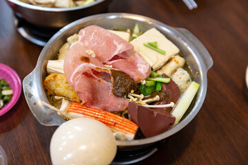 Close-up top view of Taiwanese hot pot before cooking, featuring pork slices, tofu, blood pudding, imitation crab stick, vegetables, and offal