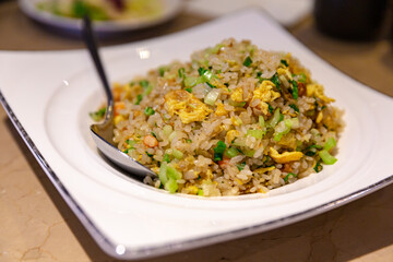 Top view of freshly served shrimp and vegetable fried rice garnished with egg, presented on a white plate with a stainless steel spoon