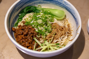 Taiwanese-style bowl of double sauce noodles, featuring a rich blend of zhajiang meat sauce and sesame paste, topped with scallions, cucumber, and bok choy