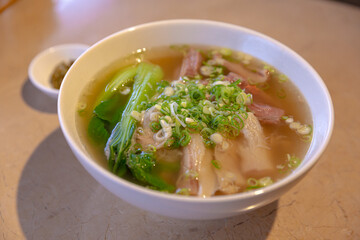 Beef brisket and tendon clear soup noodles, topped with green onions and bok choy, served in a round white bowl on a wooden table
