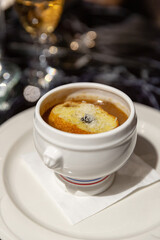 French onion soup served in a traditional white ceramic bowl, topped with toasted baguette slice and melted cheese on a formal dining table