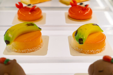 a glossy orange mousse dessert topped with a lifelike banana decoration and surrounded by shredded...