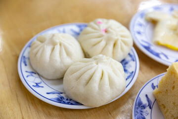 Three steamed buns placed on a traditional blue and white Chinese porcelain plate, served on a wooden table, showcasing soft fluffy texture and classic folds