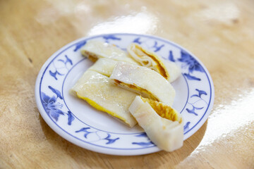 Sliced Taiwanese egg pancake made from rice flour crepe, cut into bite-sized rolls, displayed on a floral ceramic plate without sauce