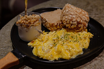 Hearty western-style breakfast with fried eggs, sausages, bread roll, and assorted sides, served on a round black plate in a cozy café setting