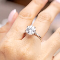 A large, round brilliant cut diamond engagement ring gleams on a hand, showcasing exquisite craftsmanship and sparkle.