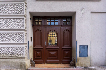 Wooden entrance door of a tenement in Poland with decorative glass and metal grille, surrounded by ornamental plaster on the building facade
