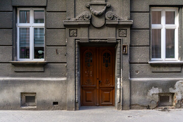Tenement house with decorative portal, wooden doors, stucco details, front facade view with windows and city sidewalk.