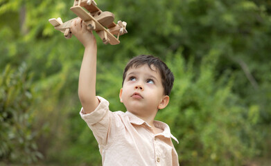 Happy family relaxing in park on summer day. Parents sit on blanket with smiling boy playing with wooden toy airplane. Father lifts child up, concept of flight, travel and joyful family moments.