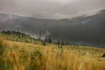 Moody mountain scene with fog and cloudy sky. Wet winding road after rain, caravan in the middle,...
