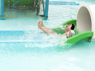 Happy preschool child slides down water slide with splashes, wearing goggles and arm floaties....