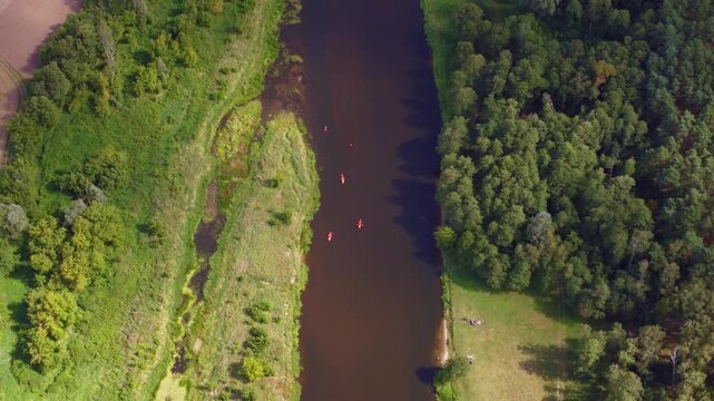 Aerial view of a river in Nowy Lubiel, Poland, with kayakers paddling downstream, open fields, dense forest, and people near the grassy area.