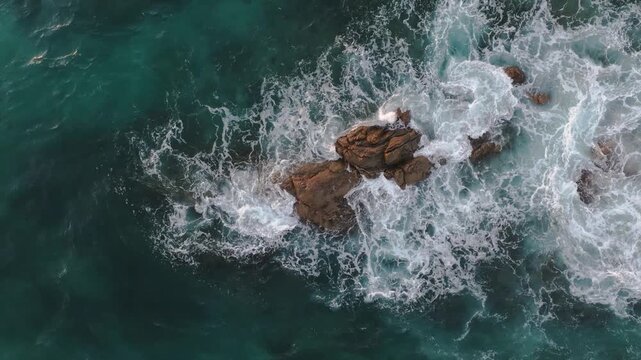 Aerial view of turquoise ocean waves crashing against the dark, jagged rocks, creating white foam patterns, Yallingup, Western Australia, Australia.