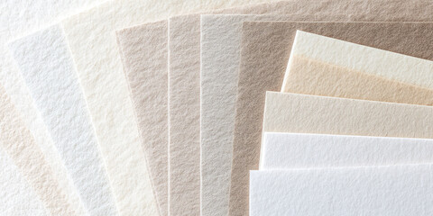 Sheets of paper are fanned out, showcasing different off-white and beige tones. Neutral tone art or stationery concept