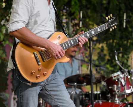 Unrecognizable rock musician playing in band playing for performance tuning golden yellow electric guitar, drummer copy space. rock band. The guitarist plays solo. Drummer. Bass drum. Close-up image.