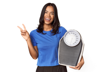 Filipino woman with scale in studio joyful and carefree showing a peace symbol with fingers.