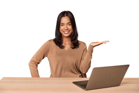 Filipino woman at desk with laptop showing a copy space on a palm and holding another hand on waist.