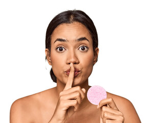 Woman holds facial sponge in studio keeping a secret or asking for silence.