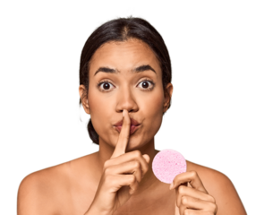 Woman holds facial sponge in studio keeping a secret or asking for silence.