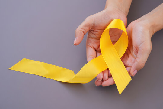 Hands holding a yellow awareness ribbon symbolizing support and hope