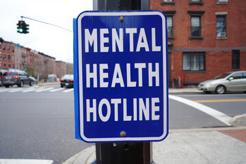 Blue sign on a pole reads mental health hotline on a city street