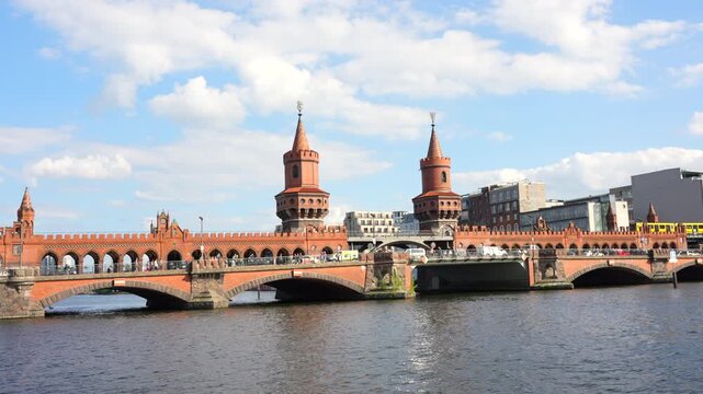 Berlin, Germany - May 30, 2025: Iconic Oberbaum Bridge in Berlin, featuring a yellow U-Bahn train crossing over the River Spree with blue skies and white clouds.