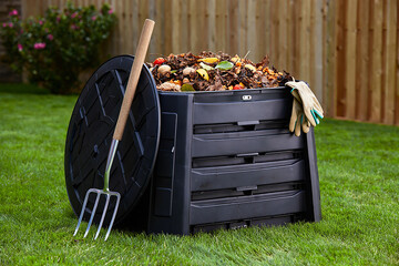 Compost bin with garden fork and gloves in a backyard
