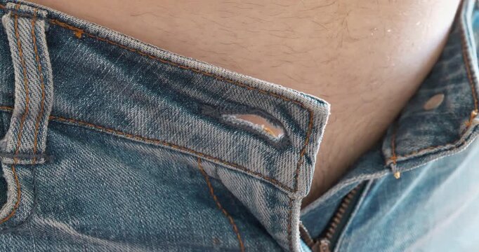Skinny jeans and a fat belly. Close-up of blue jeans and paunch, beer belly. Man was unable to button his jeans at the waist. The pants size is small and unsuitable. Trying on clothes in fitting room