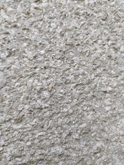 A close-up of a rough, light gray stucco wall surface with a grainy and uneven texture.