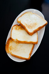 Golden slices of toasted bread, stacked on a white plate against a dark background. Warm and inviting.