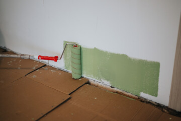 A paint roller with a red handle is used to apply green paint on a white wall for a renovation or...