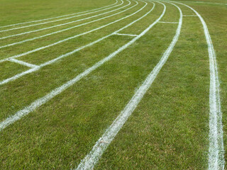 Obraz premium Athletics running track lanes. White paint lines on grass field, low angle.