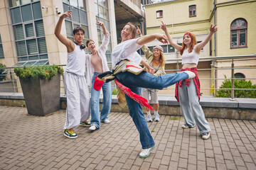 Female dancer kicking leg with joy while friends surround with laughter and style. Concept of youth...