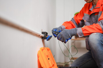 Electrician working on electrical outlet installation and maintenance in modern residential home with professional tools and safety gear