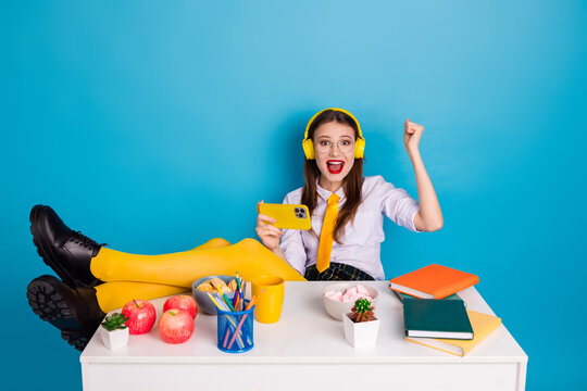 Excited college student enjoying leisure with smartphone and headphones at stylish desk with vibrant decor - Powered by Adobe