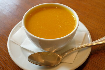 a cup of pumpkin pottage with spoon on wooden table
