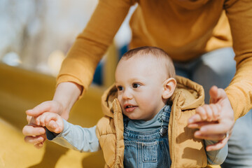 Parent enjoying a bonding moment while guiding cheerful child at a sunny playground filled with...
