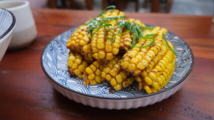 Golden fried corn ribs cut into small sections and garnished with herbs, served on a decorative ceramic plate over a wooden table.  

