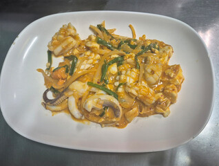 Authentic Thai spicy stir fried squid with vegetables and onions served on white plate, traditional Asian seafood cuisine with chili sauce and green chives