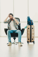 Worried male tourist talking on phone at airport terminal with suitcase waiting for journey and...