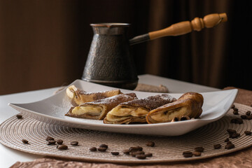 plate rolled pastries filled with sweet cream and bananas sits on table, accompanied by cup coffee....