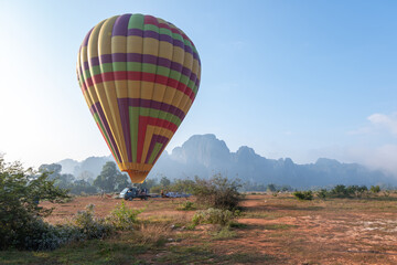 Colorful hot air balloon preparing for takeoff in open field with mountain background